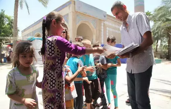 An Iraqi citizen hands out guidebooks to children on how to avoid the dangers of mines and how to avoid approaching or playing with unknown objects. Photo posted on April 4, 2022. [Iraqi Ministry of Environment]