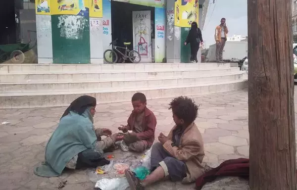 A mother and her children eat on the sidewalk outside a shopping center in Sanaa in this undated photo. The war continues to cast a shadow on all aspects of life in Yemen. [Yazan Abdul Aziz/Al-Fassel]