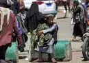 
A young pedlar sits on a concrete block while holding camouflage-patterned jacket fatigues to be sold to pedestrians along a street in Yemen's capital Sanaa on March 24, 2022. [Mohammed Huwais/AFP]        