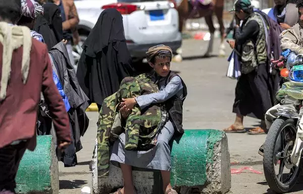 A young pedlar sits on a concrete block while holding camouflage-patterned jacket fatigues to be sold to pedestrians along a street in Yemen's capital Sanaa on March 24, 2022. [Mohammed Huwais/AFP]