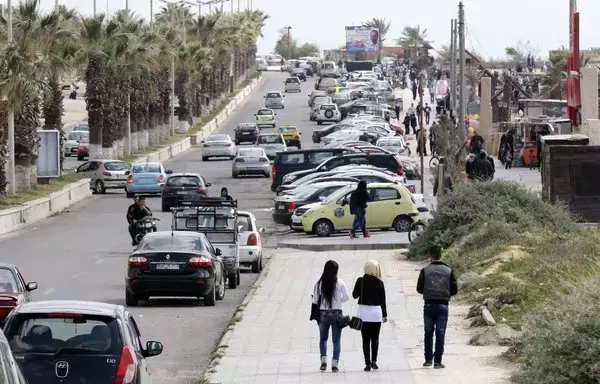 Syrians walk near the Mediterranean coast in the regime-controlled city of Latakia on March 18, 2016. [Louai Beshara/AFP]