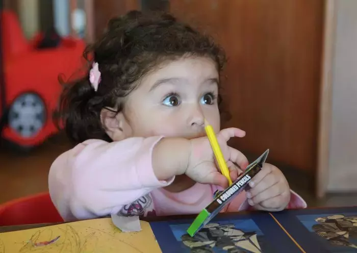 A toddler draws with colored pencils. [Naji Akram/Al-Fassel]