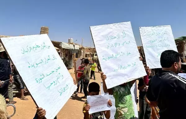 Al-Rukban camp residents hold signs denouncing the Syrian regime on September 1 in solidarity with the ongoing protests in the southern city of Sweida. [Al-Rukban Media Center]