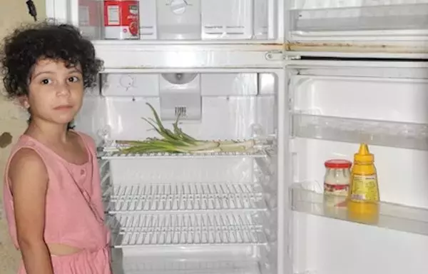 A girl stands next to an empty refrigerator in her home in the northern Lebanon city of Tripoli. [Naji Akram/Al-Fassel]