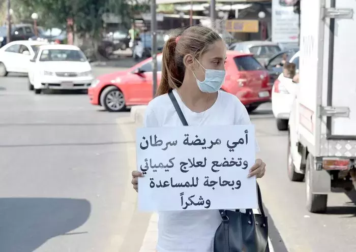 A Lebanese woman raises a sign in Beirut asking for help for her mother, who suffers from cancer and needs treatment. [Naji Akram/Al-Fassel]