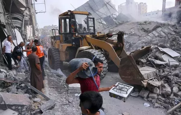 A Palestinian man carries salvageable items as civilians and rescuers help clear the rubble in the heavily bombarded city center of Khan Yunis in the southern Gaza strip following overnight Israeli shelling, on October 10. [Said Khatib/AFP]