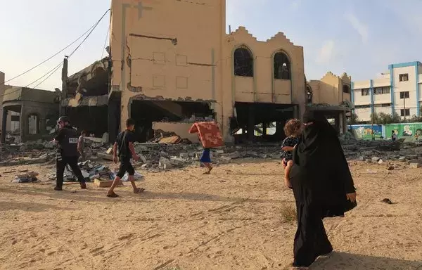 A journalist and civilians walk past a damaged building in Khan Yunis, following Israeli air strikes on the southern Gaza strip, on October 8. [Said Khatib/AFP]