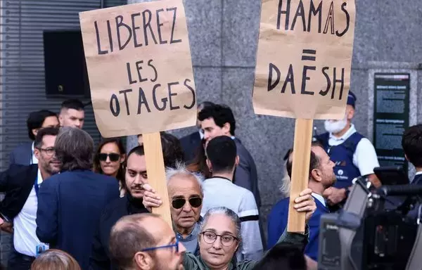 A woman holds placards reading 'Hamas=Daesh (ISIS)' and in French 'free the hostages' during a tribute to the victims of the Hamas-organized attacks in Israel, at the European Parliament in Brussels, on October 11. [Kenzo Tribouillard/AFP]