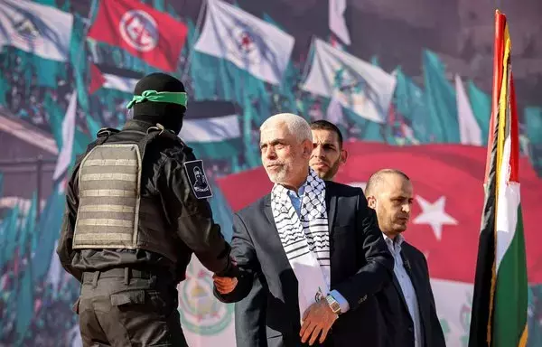 Gaza chief of Hamas Yahia al-Sinwar shakes hands with a masked fighter of the militant group's Ezzedine al-Qassam Brigades during a rally marking the 35th anniversary of its foundation, in Gaza City on December 14, 2022. [Mohammed Abed/AFP]