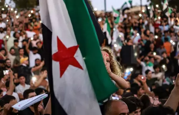 A girl raises the flag of the Syrian opposition during a demonstration in the northwestern city of Idlib on August 25, in support of anti-regime protests in the southern city of Sweida. [Abdulaziz Ketaz/AFP]