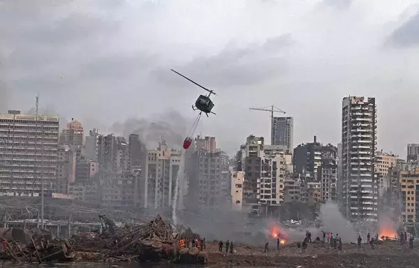 A helicopter tries to put out multiple fires at the scene of the massive explosion that hit Beirut's port on August 4, 2020, in the heart of the Lebanese capital. Some Lebanese blame Hizbullah for the explosion for storing explosive materials in the port silos. [AFP]