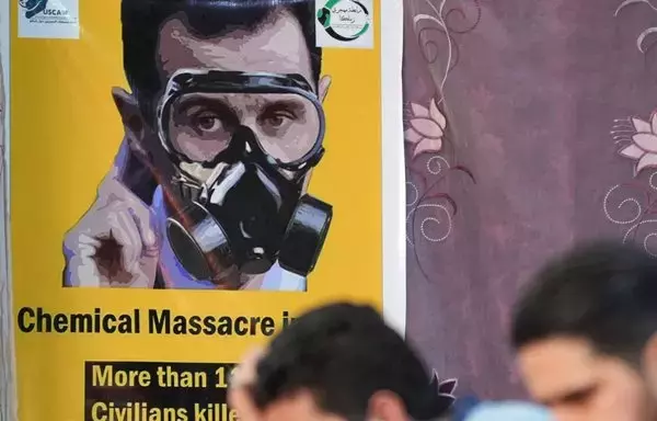 A poster depicting Syria's president Bashar al-Assad in a gas mask is seen in the opposition-held northern city of Afrin on August 20, marking the 10-year anniversary of chemical attacks that killed over 1,400 people in Eastern Ghouta, outside Damascus. [Rami al-Sayed/AFP]