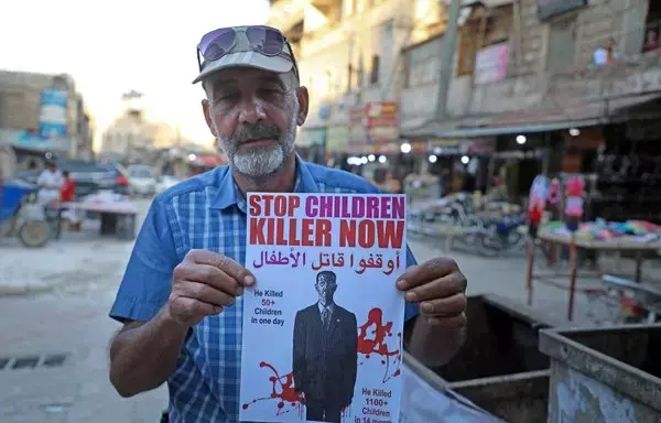 A Syrian man holds a poster depicting Bashar al-Assad as a killer in the Idlib province town of Dana on May 24, 2021. [Aaref Watad/AFP]