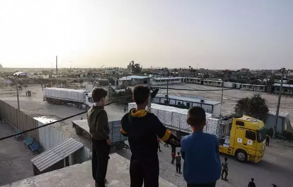 Young boys look at trucks carrying humanitarian aid entering Gaza via the Rafah crossing with Egypt on November 26, the third day of a truce between Israel and Hamas. [Mohammed Abed/AFP]