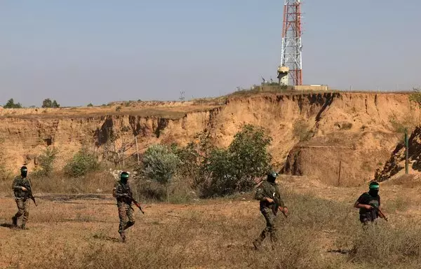 Fighters of the Ezzedine al-Qassam Brigades, the armed wing of Hamas, walk past an Israeli army position and surveillance antenna, during a July 19 military parade near the border. [Mahmud Hams/AFP]