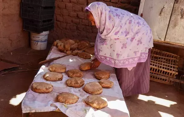 Egyptian Naamat Jabal Sayyid Hasan, 75, bakes bread in a mud hut as she does daily to offer to people fleeing war-torn Sudan passing through in the northern town of Wadi Halfa near the border with Egypt, on April 29. [Ashraf Shazly/AFP]