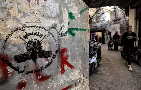 A woman walks along an alley near graffiti showing the logo of the Palestinian Islamic Jihad (PIJ) movement at the Shatila camp for Palestinian refugees in the southern suburb of Beirut on November 7, amid ongoing battles between Israel and the Palestinian terrorist group Hamas in Gaza. [Ahmad al-Rubaye/AFP]