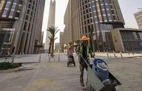 Chinese construction workers push carts at the site of ongoing work at the Central Business District in Egypt's New Administrative Capital megaproject about 45km east of Cairo on August 1. The 'Iconic Tower' skyscraper, currently under construction and expected to reach an elevation of 394 meters, is seen in the background. [Khaled Desouki/AFP]