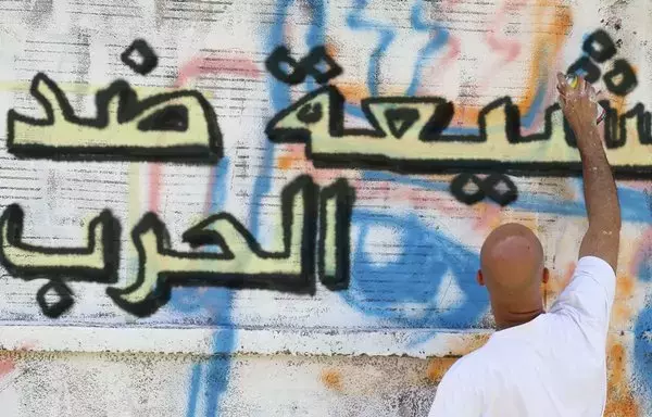 A man spray paints graffiti art on a wall in Lebanon that says: "Shias are Against War." [Shias Against War Facebook page]