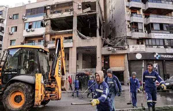 عمال بلدية ينظفون الشارع يوم 3 كانون الثاني/يناير أمام مبنى في الضاحية الجنوبية ببيروت حيث قتل نائب رئيس حركة حماس صالح العاروري في ضربة بمسيرة قبل يوم. [أنور عمرو/وكالة الصحافة الفرنسية]