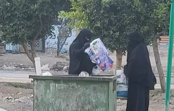 Women in Sanaa's Bayt Baws neighborhood search a dumpster for leftover food. [Yazan Abdulaziz/Al-Fassel]