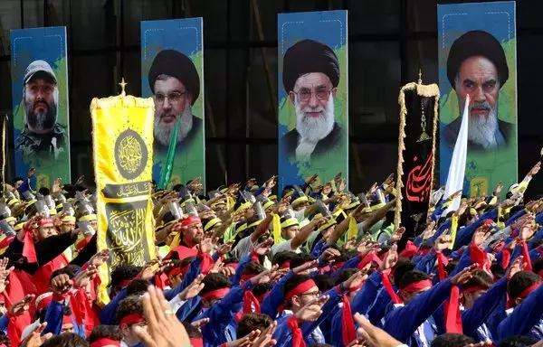 Scouts loyal to Hizbullah salute during a procession in Lebanon's southern city of Nabatiyeh on August 12, 2022, as they march past posters of Hizbullah's slain military leader Imad Moghniyeh, current leader Hassan Nasrallah, Iran's leader Ali Khamenei and late supreme leader Rouhollah Khomeini. [Mahmoud Zayyat/AFP]