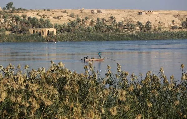 A picture taken from the Iraqi border town of al-Qaim on November 13, 2018, shows a fishing boat in the Euphrates river, with the Syrian border town of Albu Kamal on the other side. [Ahmad al-Rubaye/AFP]