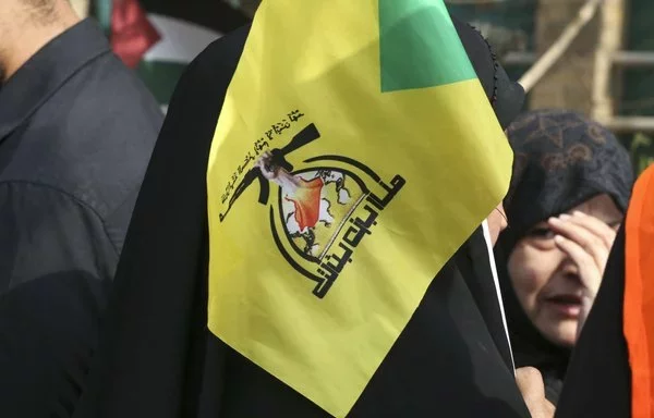 An Iraqi woman lifts a Kataib Hizbullah flag during a rally on Baghdad's Aba Nawas street on April 29, 2022. [Sabah Arar/AFP]