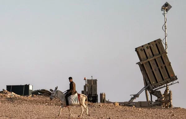 A boy rides a donkey near one of the batteries of Israel's Iron Dome missile defense system in the southern Negev desert on April 14. [Ahmad Gharabli/AFP]