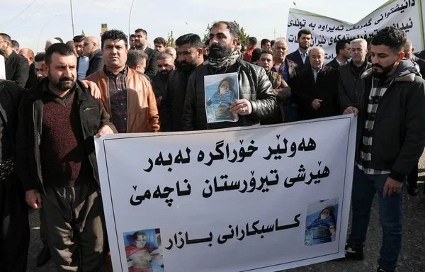 Protesters hold pictures of children's bodies and a banner reading 'Erbil remains resilient, and it does not kneel down to terrorist attacks' during a demonstration January 16 outside the United Nations (UN) office in Erbil, a day after several areas in the city were hit by a missile attack launched by Iran's IRGC. [Safin Hamid/AFP]