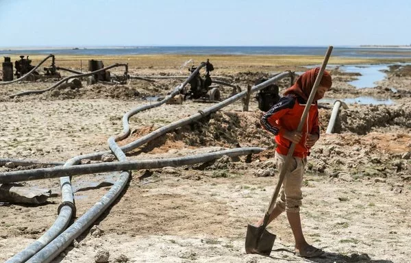 A youth walks near water pumps drawing water from the Lake Assad reservoir, in the village of al-Tuwayhinah near the Tabqa Dam along the Euphrates river in al-Raqa province on July 27, 2021. [Delil Souleiman/AFP]