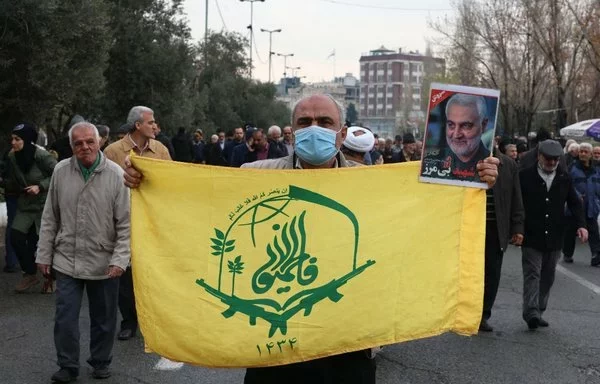 The flag of the IRGC-controlled Fatemiyoun Division, a militia comprised of Afghan fighters formed in 2014 to fight in Syria, is carried through Tehran on January 12, with a portrait of the late IRGC Quds Force commander Qassem Soleimani. [AFP]