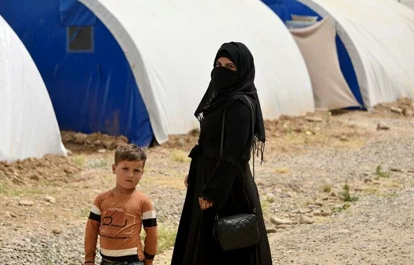 A woman and child stand near tents at al-Jadaa camp in Iraq, which houses families repatriated from Syria's al-Hol camp, on April 29. Families undergo psychological rehabilitation at al-Jadaa. [Zaid al-Obeidi/AFP]