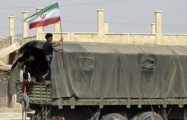 A Syrian boy holds the Iranian flag atop a truck carrying aid in the eastern city of Deir Ezzor on September 20, 2017. [Louai Beshara/AFP]