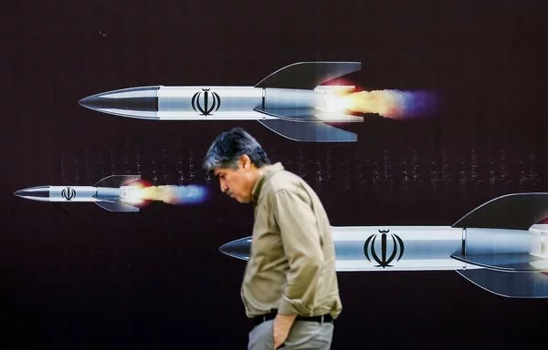 A man walks past a banner depicting missiles along a street in Tehran on April 19. [AFP]