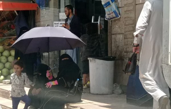 A woman sits on a sidewalk with her two children in Sanaa's Bayt Baws neighborhood. [Yazan Abdul Aziz/Al-Fassel]