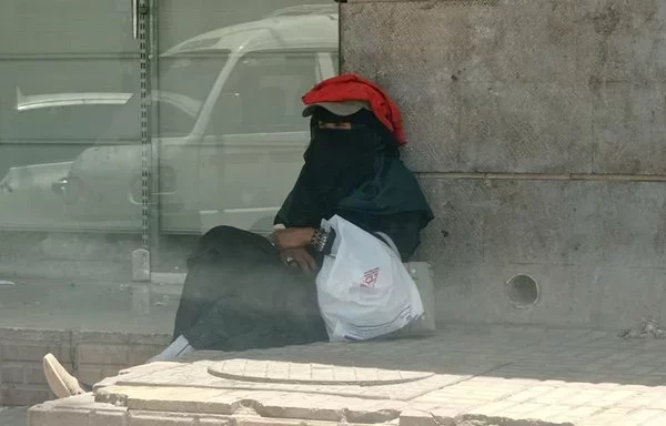 A woman sits on a sidewalk in Houthi-controlled Sanaa. [Yazan Abdul Aziz/Al-Fassel]