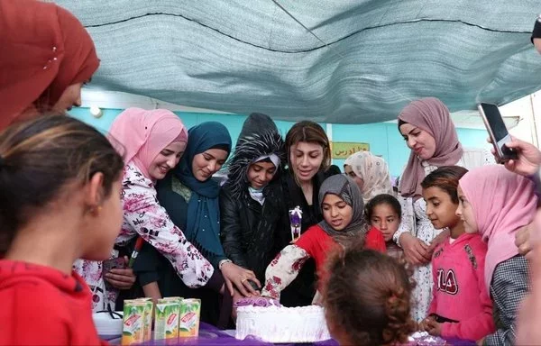 وزيرة الهجرة العراقية إيفان جابرو تقطع كعكة مع مجموعة من الفتيات في مركز الجدعة المخصص للتأهيل بالقرب من الموصل يوم 9 آذار/مارس. [حساب إيفان جابرو على موقع إكس].