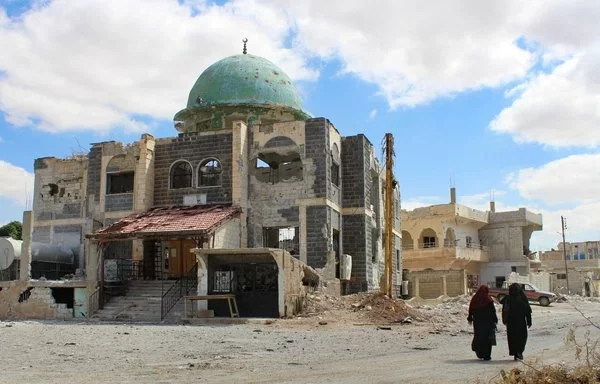 Women walk past a damaged mosque in Daraa's Daraa al-Balad district on September 11, 2021. [Sam Hariri/AFP]