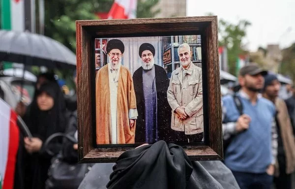 A demonstrator in Tehran holds a photo of Iranian leader Ali Khamenei, late Hizbullah leader Hassan Nasrallah, and late IRGC Quds Force commander Qassem Soleimani, on September 28. [Atta Kenare/AFP]