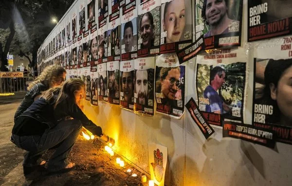 Candles are lit in Jerusalem on November 7, 2023, beneath posters of hostages abducted by Hamas. [Ahmad Gharabli/AFP]