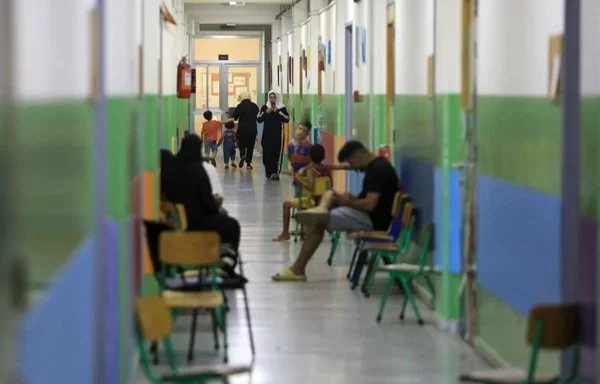 People sit in a corridor at a school housing families displaced from the south of Lebanon, in Beirut on October 5. [AFP]