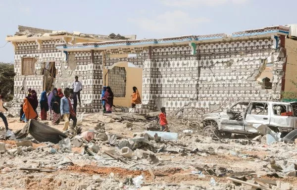 People stand beside a destroyed house and the wreckage of a car following an al-Shabaab attack on a police station on the outskirts of Mogadishu, Somalia, on February 16, 2022.[Hassan Ali Elmi/AFP]