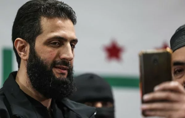 A man takes a picture with his mobile phone of Syria's de facto new leader, Ahmed al-Sharaa, previously referred to as Abu Mohammed al-Joulani, on March 12, 2024. [Omar Haj Kadour/AFP]