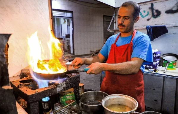 A cook prepares an order at a street food restaurant in Houthi-controlled Sanaa on December 26, 2021. The Houthis have sought to restrict the import of cooking gas from government-controlled Marib in favor of imports through al-Hodeidah port, which they control. [Mohammed Huwais/AFP]