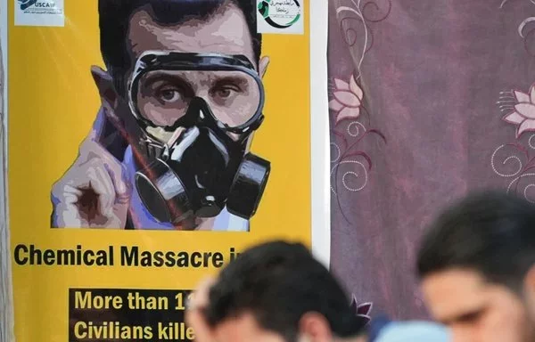 Bashar al-Assad wears a gas mask in a poster displayed in Afrin on August 20, 2023, during a 10th anniversary commemoration of deadly chemical attacks in Eastern Ghouta. [Rami al Sayed/AFP]